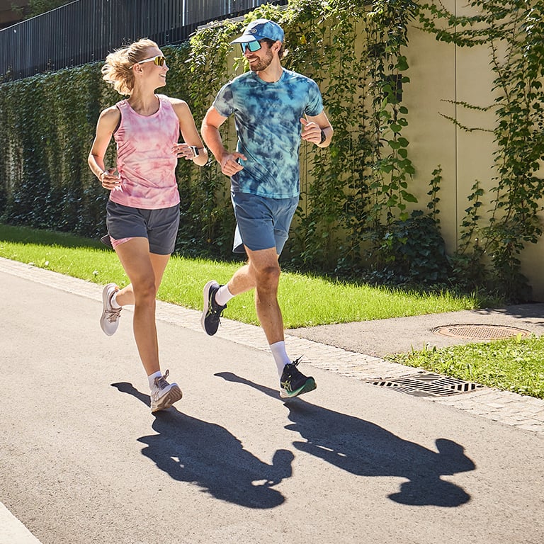 Zwei Personen in sommerlicher Laufbekleidung joggen an nemen einem Grünstreifen.
