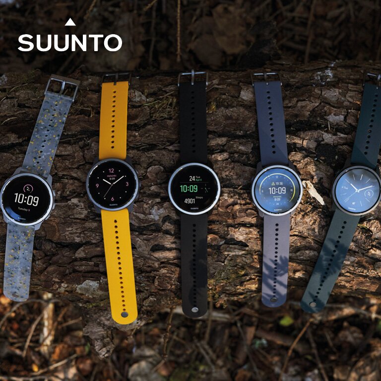 Suunto. Sechs Sportuhren in verschiedenen Farben liegen auf einem Baumstamm.