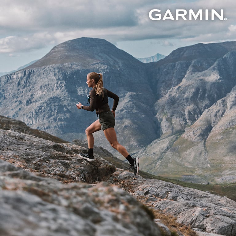 Garmin - Eine Frau läuft mit ihrem Trailrunning Outfit den Berg hinauf.