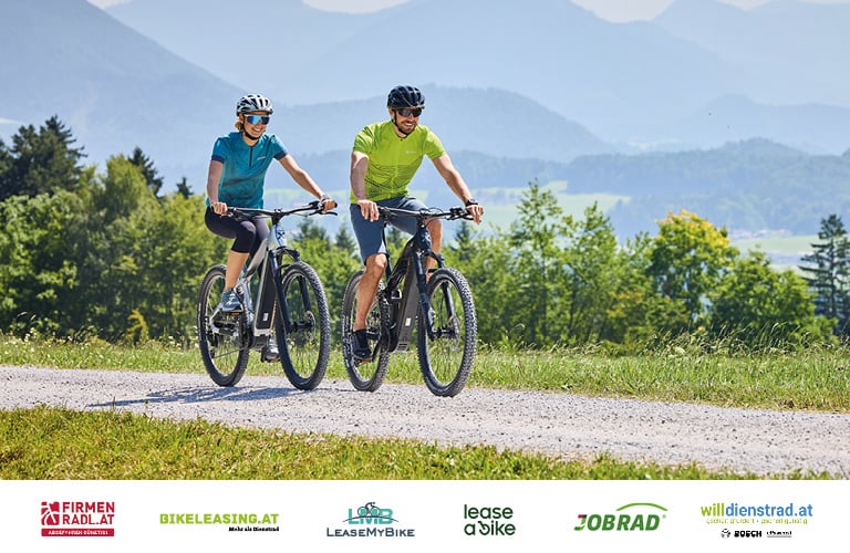 Zwei Personen radlen auf einem Schotterweg. Unterhalb sind die Logos von Firmenradl.at, Lease My Bike, Bikeleasing.at, Jobrad, lease a bike und willdienstrad.at zu sehen.