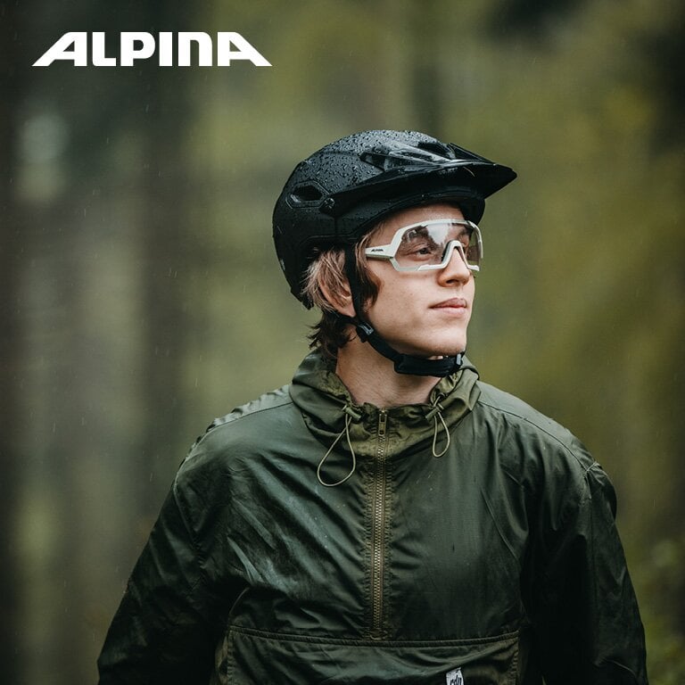Alpina. Ein junger Mann trägt einen schwarzen Alpina Fahrradhelm und eine weiße Sportbrille.