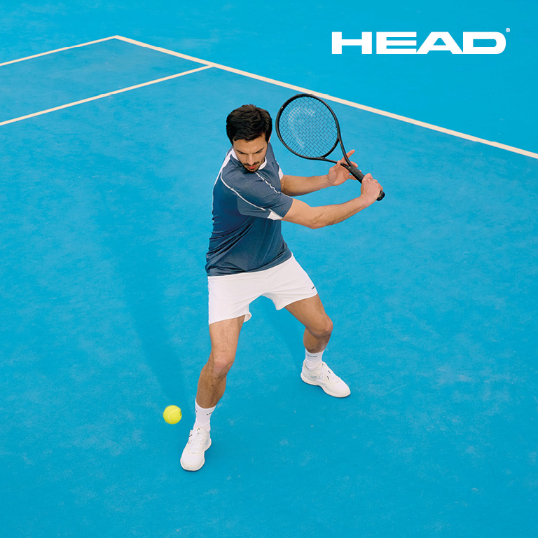 Eine Person bereitet auf einem blauen Tennisplatz einen Rückhandschlag vor. Rechts oben im Bild ist das HEAD‑Logo zu sehen.
