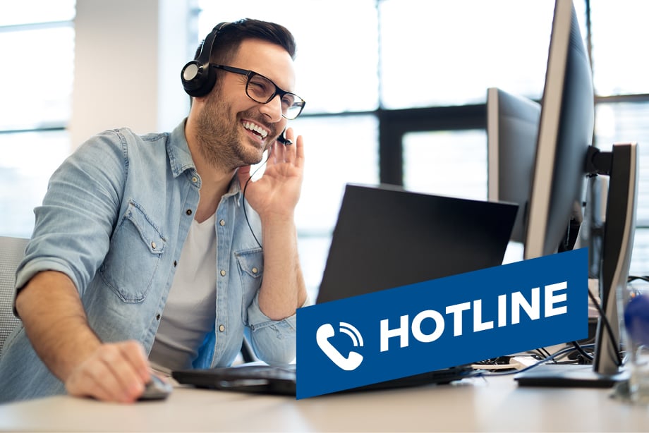 Ein Mann sitzt an einem Schreibtisch und trägt ein Headset. Vor ihm steht ein Laptop. Auf dem Bild ist ein blaues Schild mit der Aufschrift Ein Mann sitzt an einem Schreibtisch und trägt ein Headset. Vor ihm steht ein Laptop. Auf dem Bild ist ein blaues Schild mit der Aufschrift