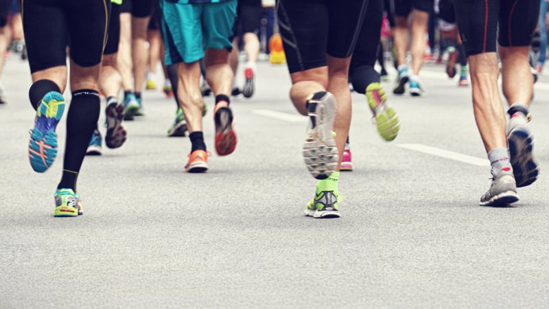 Laufberater Gruppe von Läuferinnen und Läufern bei einem Rennen oder Marathon. Der Fokus liegt auf den Beinen und Füßen in Bewegung, verschiedene Laufschuhe sind auf dem Asphalt sichtbar