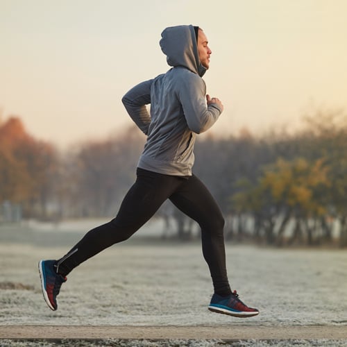 Mann joggt in sportlicher Kleidung durch eine herbstliche Landschaft.