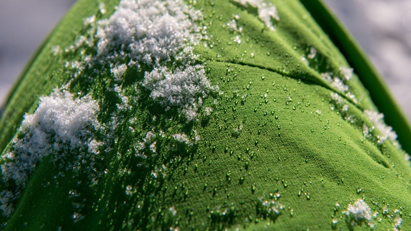 Nahaufnahme eines grünen Stoffes mit Wassertropfen und Schneeflecken auf der Oberfläche