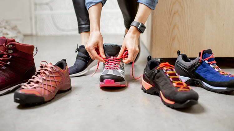 Outdoorberater Person zieht Wanderschuhe an, umgeben von weiteren Wanderschuhen in verschiedenen Designs.