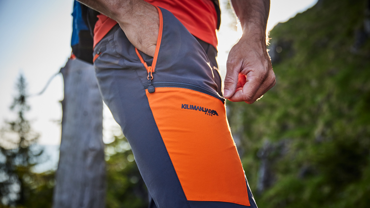 Nahaufnahme einer Outdoorhose mit seitlichem Reißverschluss und Kilimanjaro-Logo in Waldumgebung.