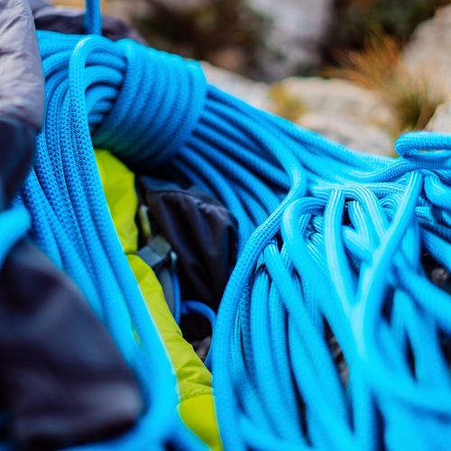 Nahaufnahme mehrerer aufgerollter blauer Seile, vermutlich Kletterseile. Im Hintergrund ist teilweise Outdoor-Ausrüstung zu erkennen.