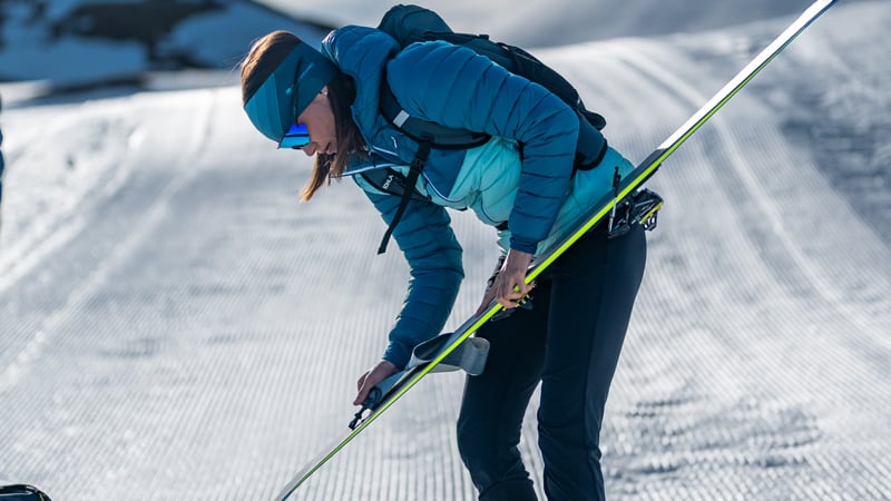 Eine Frau befestigt bei einer Skitour ein Steigfell an ihrem Ski.