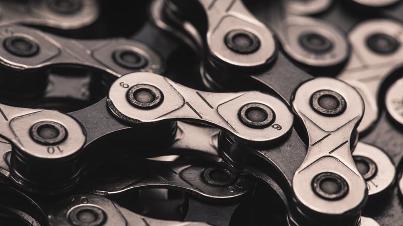 Nahaufnahme einer Fahrradkette mit metallischen, miteinander verbundenen Gliedern. Einige Glieder sind mit Zahlen wie „6“ und „10“ graviert. Die Details und Texturen der Kettenkomponenten sind deutlich sichtbar.