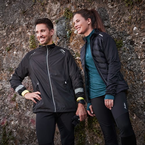 Laufbekleidung Winter Kaufberatung Mann und Frau in sportlicher Kleidung lehnen entspannt an einer Felswand.