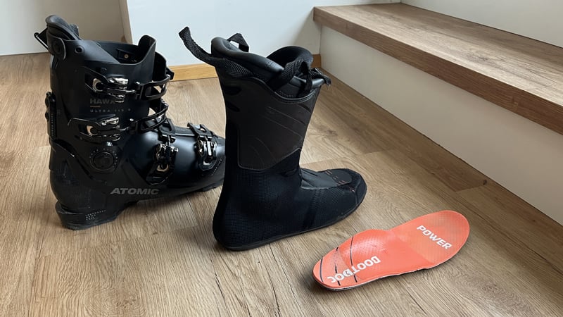 Zwei Paar Skischuhe stehen geöffnet und gut belüftet nebeneinander auf einem Holzboden