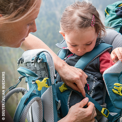 Erwachsener sichert Kind in einem Kindertragerucksack für Wanderungen.