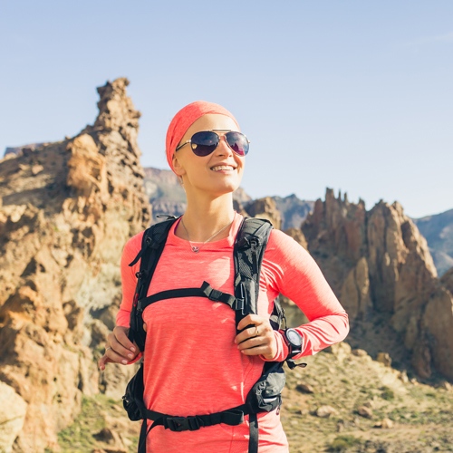 Person mit pinkem Langarmshirt und schwarzem Rucksack in felsiger Berglandschaft.