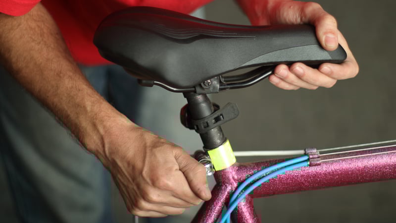 Person justiert den Fahrradsattel am Sitzrohr. Das Fahrrad hat einen glitzernden pinken Rahmen und blaue Kabel, die entlang des Rahmens verlaufen.