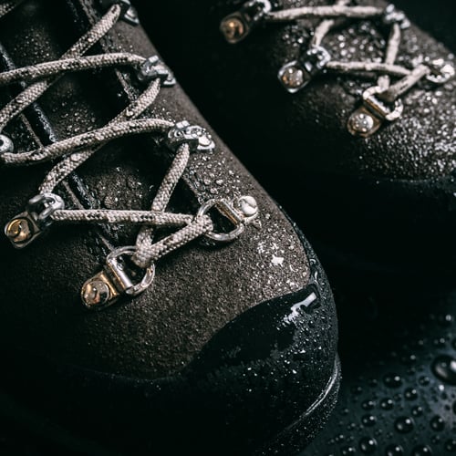 Nasse Wanderschuhe mit grauen Schnürsenkeln und Wassertropfen auf der Oberfläche.

