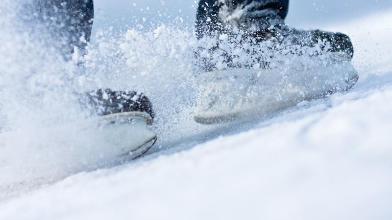 Ein Eisläufer bremst auf dem Eis und wirbelt dabei Schnee auf.