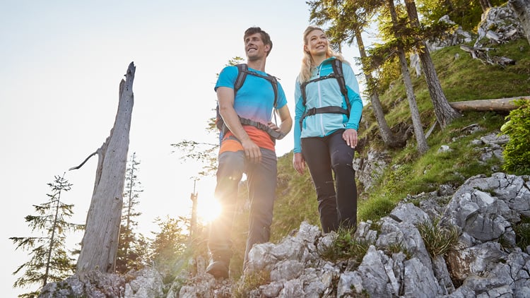 Zwei Wanderer auf felsigem Hang bei Sonnenlicht, umgeben von Natur