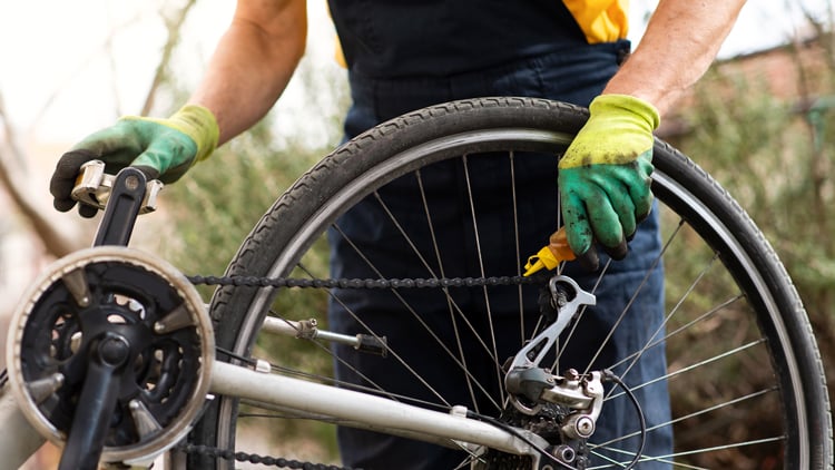 Person mit grünen Handschuhen schmiert die Fahrradkette an einem umgedrehten Fahrrad.