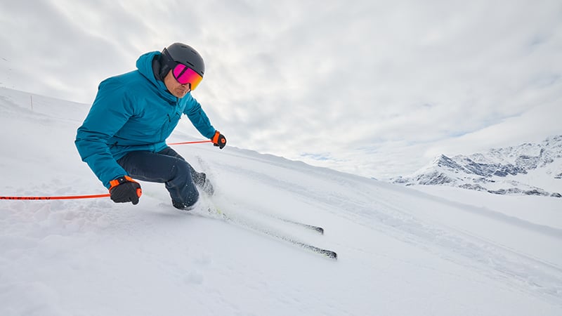 Ein Skifahrer in blauer Jacke fährt mit hoher Geschwindigkeit eine verschneite Piste hinunter.