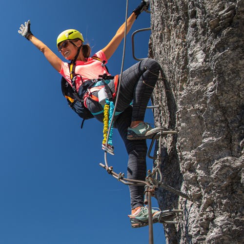 Person beim Klettern an einer Felswand mit Klettersteigausrüstung, einschließlich Helm und Gurt.