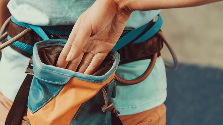 Nahaufnahme einer Person, die einen Klettergurt trägt und in einen Chalkbag greift.