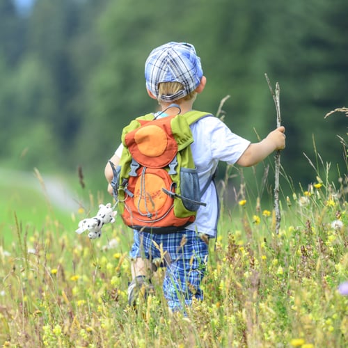Kind von hinten das mit einem Rucksack durch eine Wiese läuft