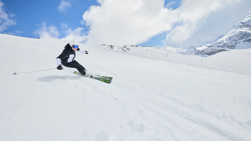 Ein Skifahrer legt auf einer breiten Piste eine enge Kurve in den Schnee.