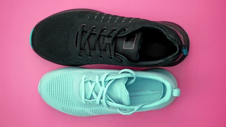 Zwei Turnschuhe nebeneinander auf pinkem Hintergrund: oben ein schwarzer Schuh mit schwarzen Schnürsenkeln und türkisfarbener Spitze, unten ein hellblauer Schuh mit passenden Schnürsenkeln und Sohle