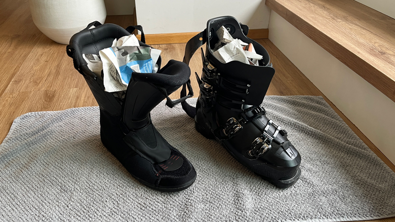 Skischuhe trocknen Schwarze Skischuhe mit herausgenommenem Innenschuh stehen auf einem Teppich, beide mit Papier ausgestopft zum Trocknen und Lüften.