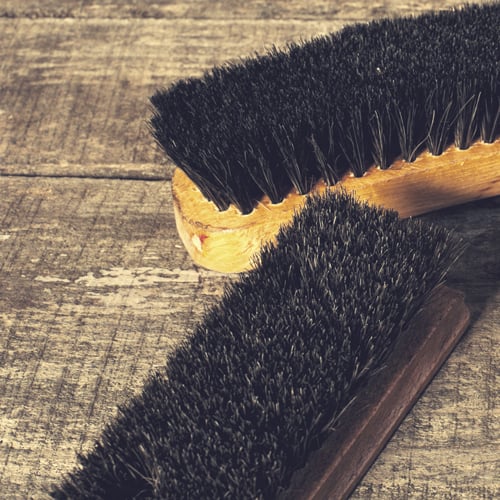 Zwei schwarze Bürsten mit Holzgriffen auf rustikalem Holztisch.