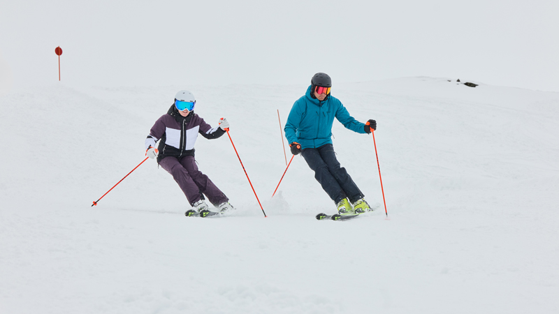 Zwei Skifahrer fahren parallel eine verschneite Piste hinunter