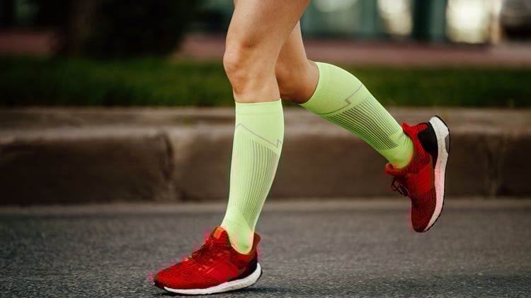 Beine eines Läufers mit roten Laufschuhen und neongelben Kompressionsstrümpfen auf der Straße.