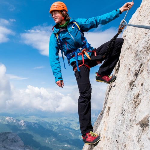 Person beim Klettern an einer Felswand mit Klettersteigausrüstung, einschließlich Helm und Gurt.