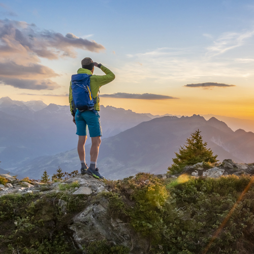 Person steht mit kurzer Wanderhose am Berggipfel und genießt den Ausblick