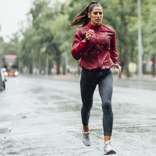 Regenjacke Kaufberatung Frau joggt bei Regen auf nasser Straße in sportlicher Kleidung.