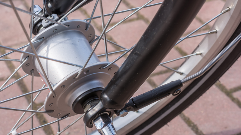 Nahaufnahme eines Fahrradlaufrads mit silbernem Nabendynamo in der Radnabe. Umgeben von Speichen, mit sichtbarer schwarzer Fahrradgabel sowie Teilen von Reifen und Felge.
