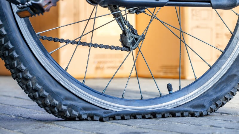 Nahaufnahme eines Fahrradreifens mit sichtbarem Platten. Der Felgenrand liegt auf dem Boden auf.