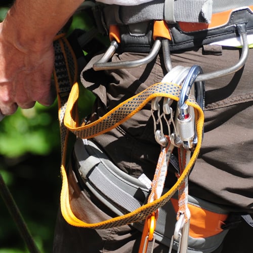 Nahaufnahme einer Person mit Kletterausrüstung. Der Klettergurt ist um Taille und Oberschenkel befestigt und mit mehreren Karabinern und Gurten ausgestattet.