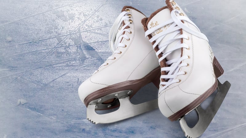 Ein Paar weiße Eislaufschuhe liegt auf einer zerkratzten Eisfläche.