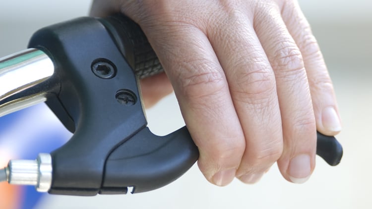 Nahaufnahme einer Hand am  Lenker eines Fahrrads; die Hand greift den Bremshebel.