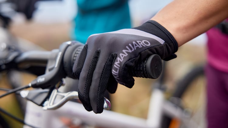 Nahaufnahme einer Hand mit schwarzem und grauem Handschuh mit der Aufschrift ‚KILIMANJARO‘, die die Bremse eines Fahrrads greift.