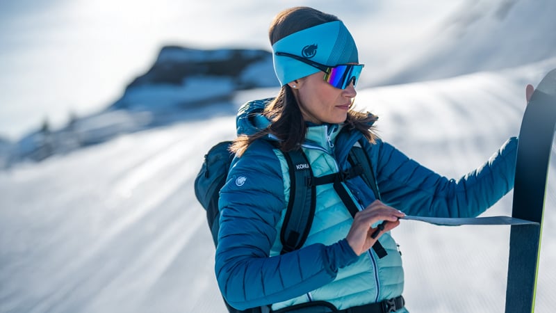 Eine Frau mit Skitourenausrüstung zieht im Schnee ein Steigfell von ihrem Ski ab.