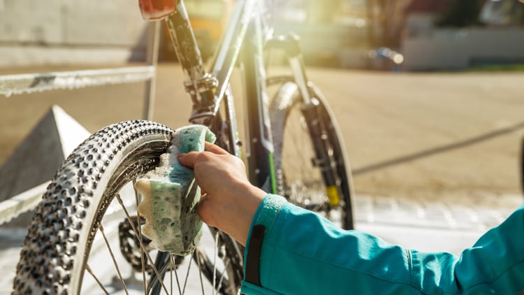 Reinigung & Pflege von Fahrrädern Person reinigt im Freien das hintere Fahrradreifenprofil mit einem Schwamm; Fokus liegt auf der Hand und dem Reifen, während der Hintergrund leicht verschwommen ist.