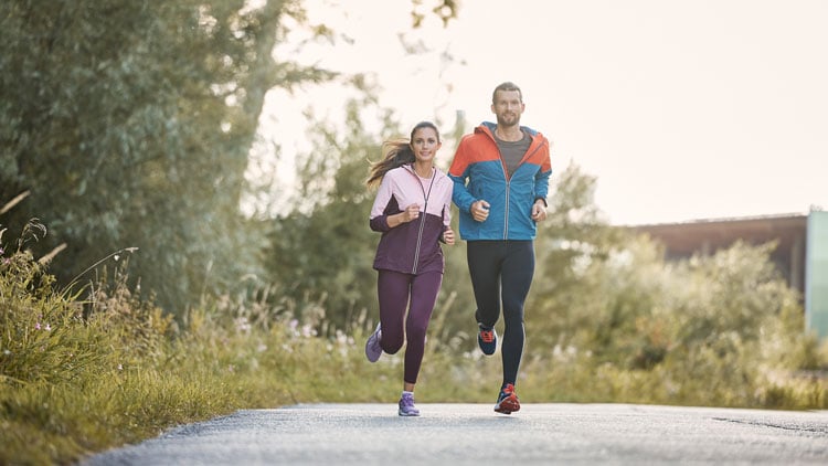 Mann und Frau joggen in sportlicher Kleidung durch eine grüne, bewachsene Landschaft